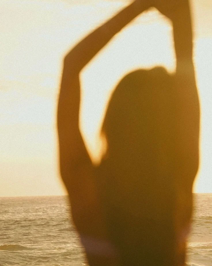 A figure stretching against a bright sea at sunset